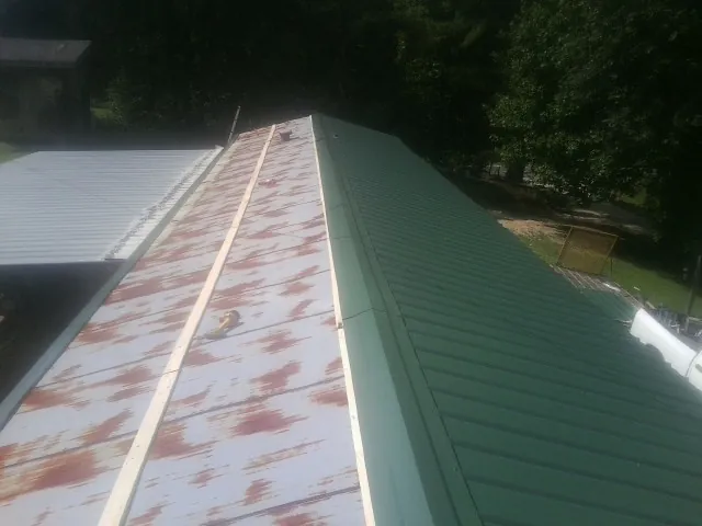 Old rusted panels beside newly installed green metal roofing — Wind Damage Roof Repair by Roofing Brothers in Constable