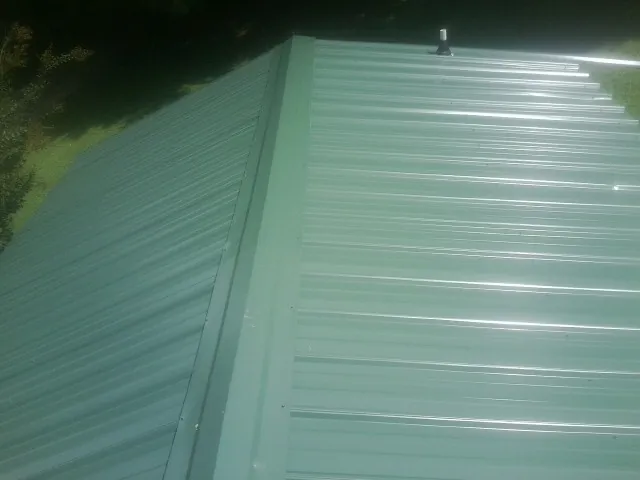 New green metal panels meeting at the ridge of a roof — Flat Roof Repair work by our crew in Constable