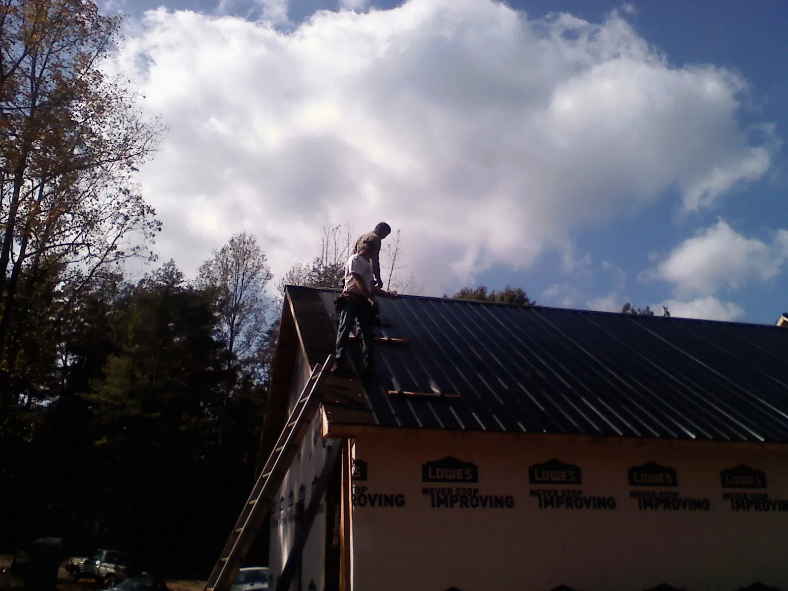 Roofer fastening dark metal panels high against a cloudy sky, from a Roof Inspection job in Constable